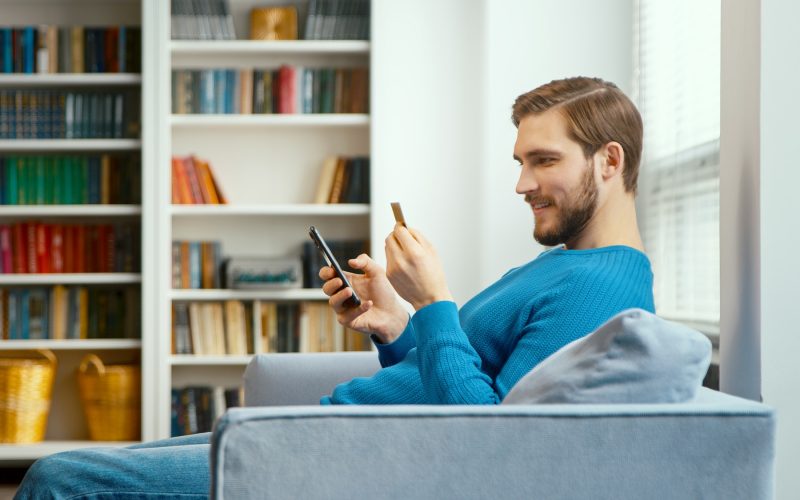 Young man looks at bank card in hand and enters digits to smartphone