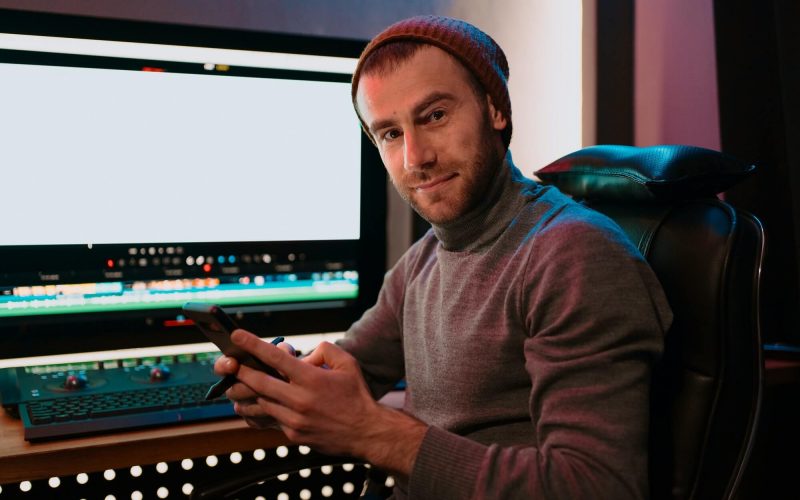 male-video-editor-sitting-at-his-computer-using-phone
