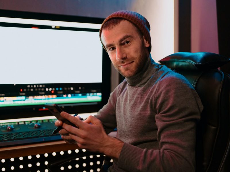 male-video-editor-sitting-at-his-computer-using-phone