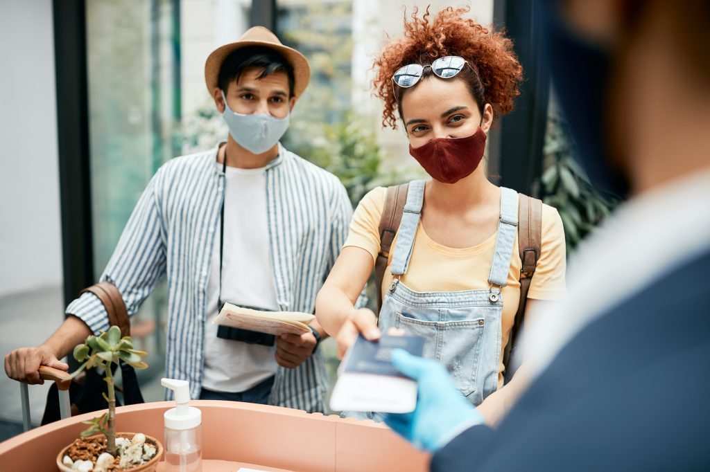 Young traveling couple wearing protective face mask during check-in at hotel reception.