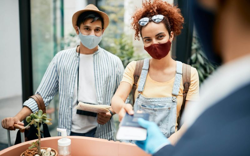 young-traveling-couple-wearing-protective-face-mask-during-check-in-at-hotel-reception-