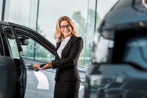 attractive smiling female car dealer opening car in showroom