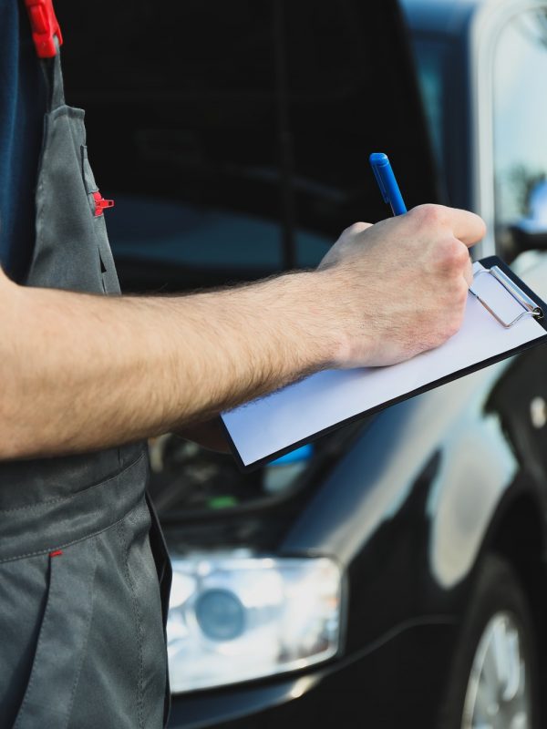 A man in overalls writes to a clipboard. Mechanic. Car inspection