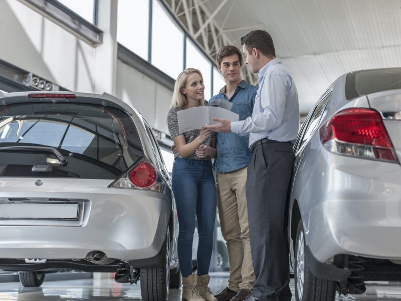Car dealer showing brochure to young couple in showroom