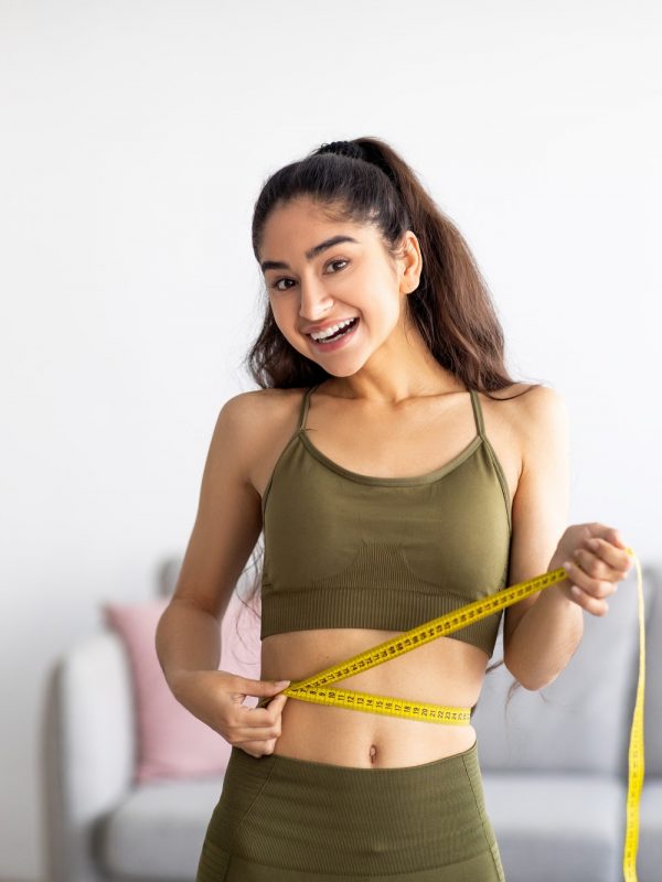 Successful weight loss. Slim Indian woman measuring waist with tape, satisfied with slimming program
