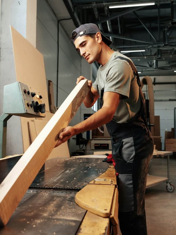 Young carpenter working on woodworking machines in the furniture factory
