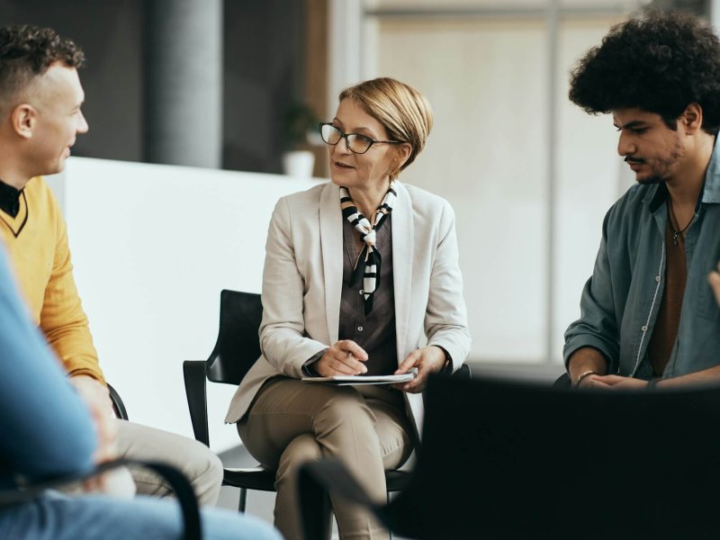 Mature therapist talking to participants of group therapy at mental health center.
