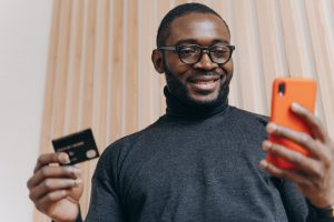 Cheerful African american businessman holding credit card and smartphone for shopping in internet