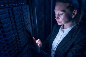 Woman engineer working in datacenter by server storage racks