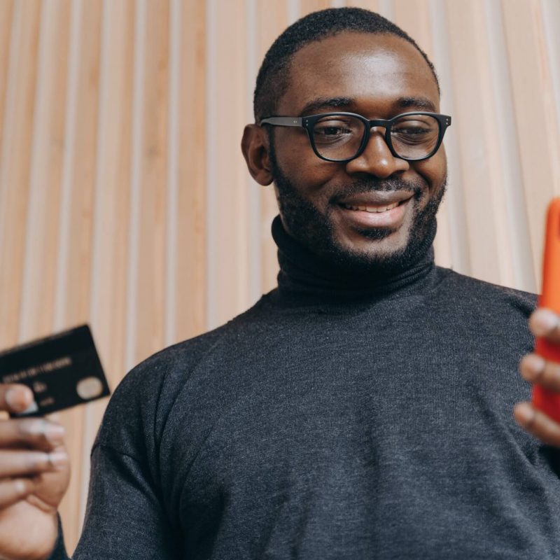 cheerful-african-american-businessman-holding-credit-card-and-smartphone-for-shopping-in-internet